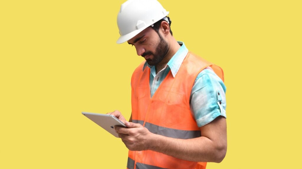 A person wearing a hard hat and looking at a tablet