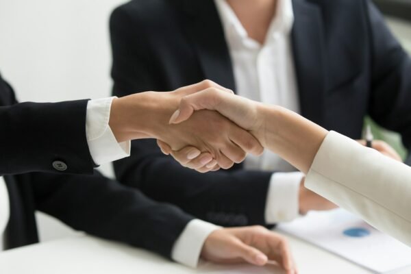 Two people shaking hands in front of a laptop