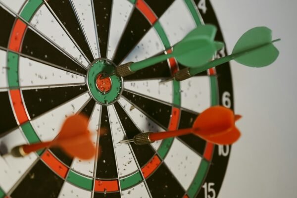 A dartboard with two green darts and one orange dart embedded in it