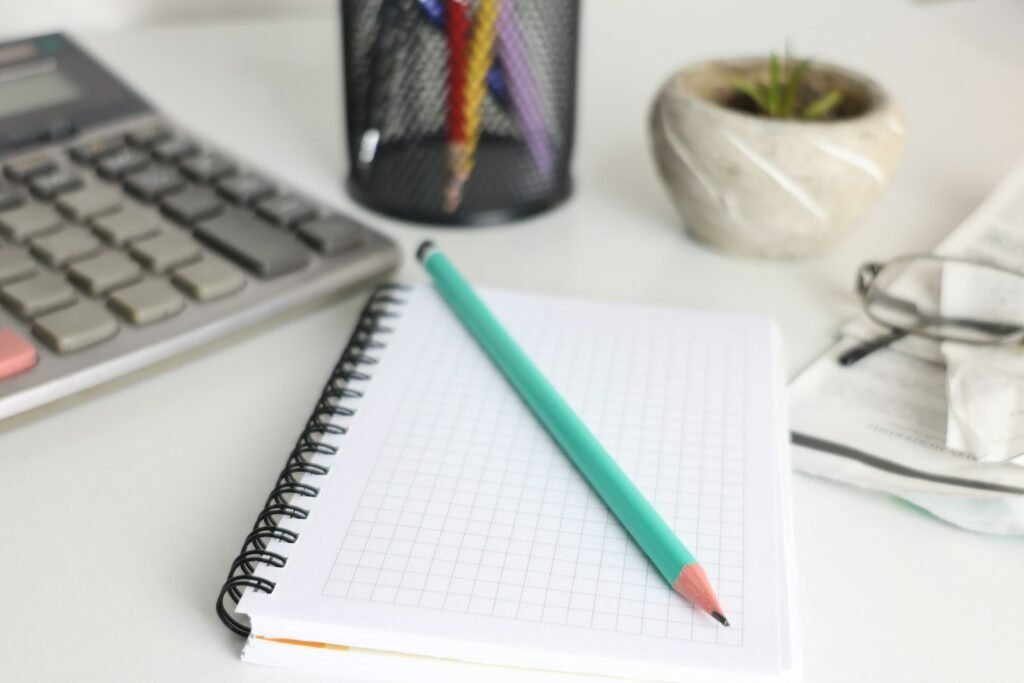 Calculator, squared notebook and pencil on a white desk, ready for working out client portal cost