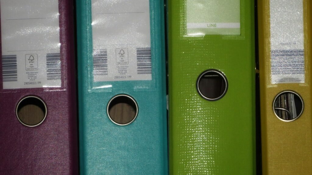 Spines of four colourful lever arch files with labels and finger holes, side by side