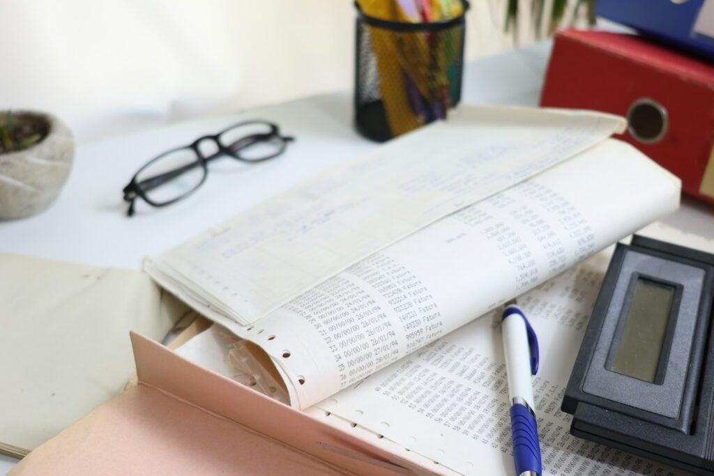 Printed ledgers and paper business records on a desk beside a calculator and glasses