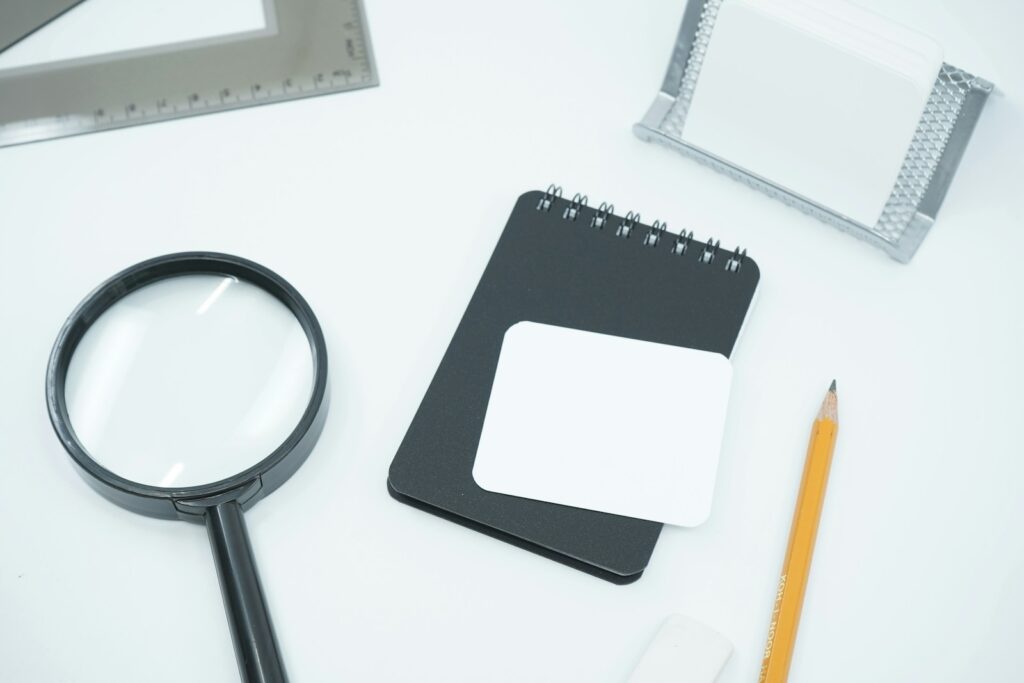 A magnifying glass, notebook and pencil on a white desk, ready for data cleansing checks