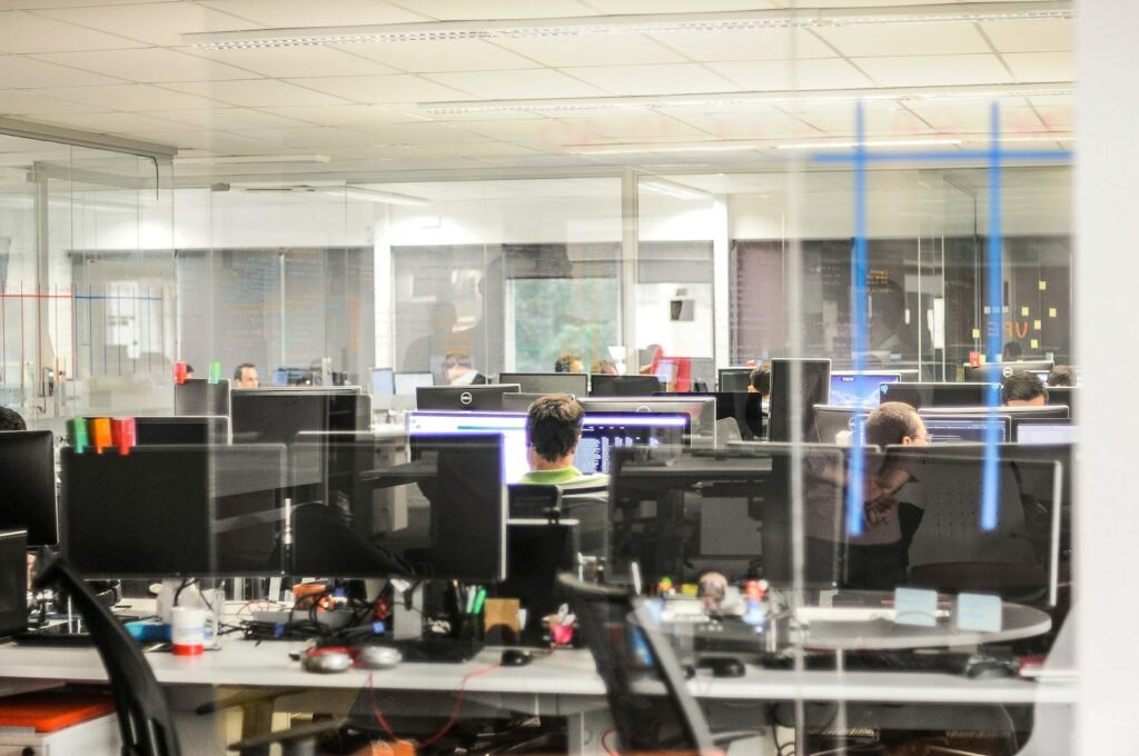 Staff working at desktop computers in an open-plan office, seen through a glass partition