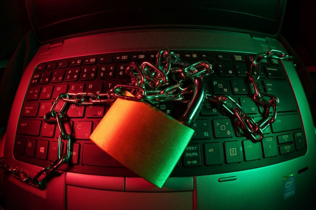 A brass padlock and chain on a laptop keyboard lit in red and green