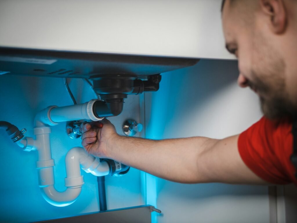 A plumber fixing a waste pipe under a sink, typical work logged in job management software
