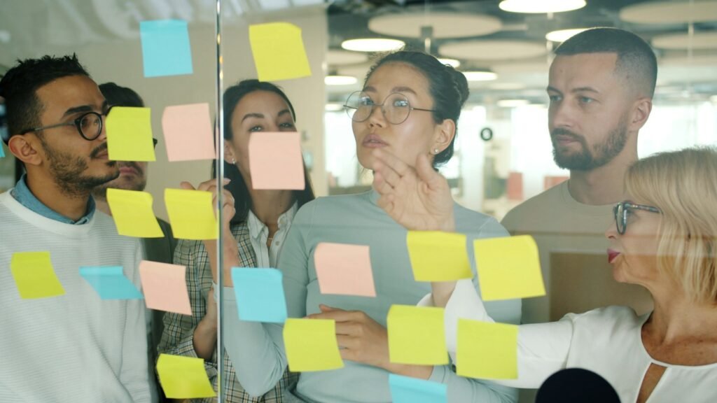 A small team arranging coloured sticky notes on a glass wall during a planning session