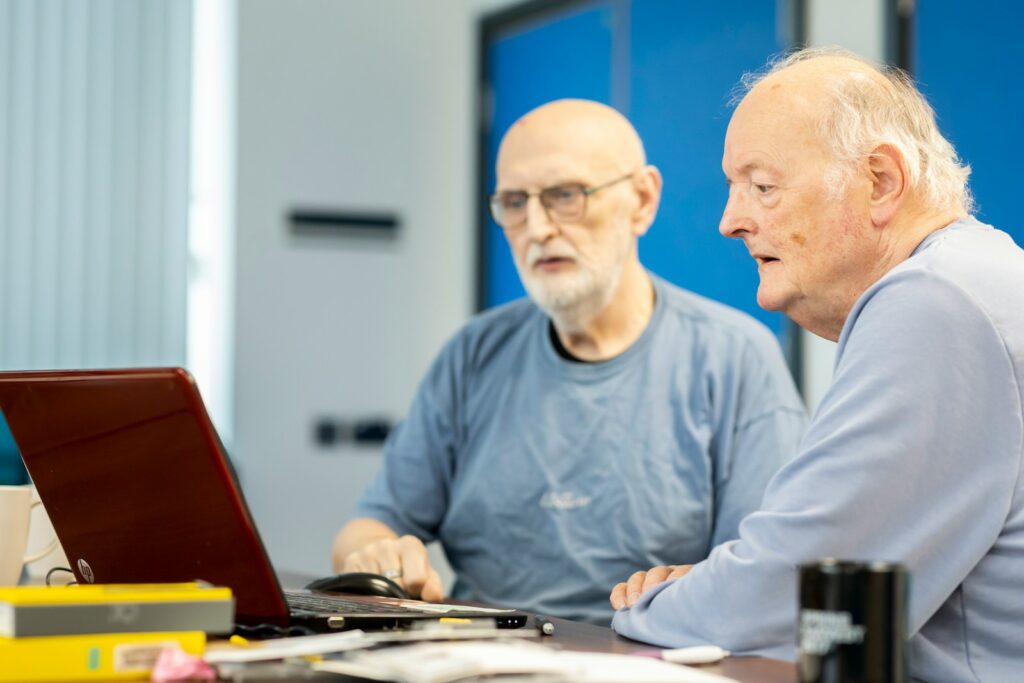 Two older men sitting at a table, looking at a laptop screen together