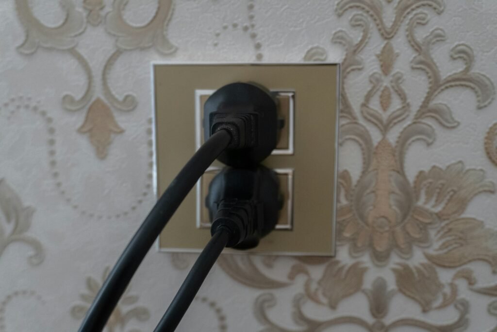 Two black plugs inserted into a gold double wall socket on patterned wallpaper