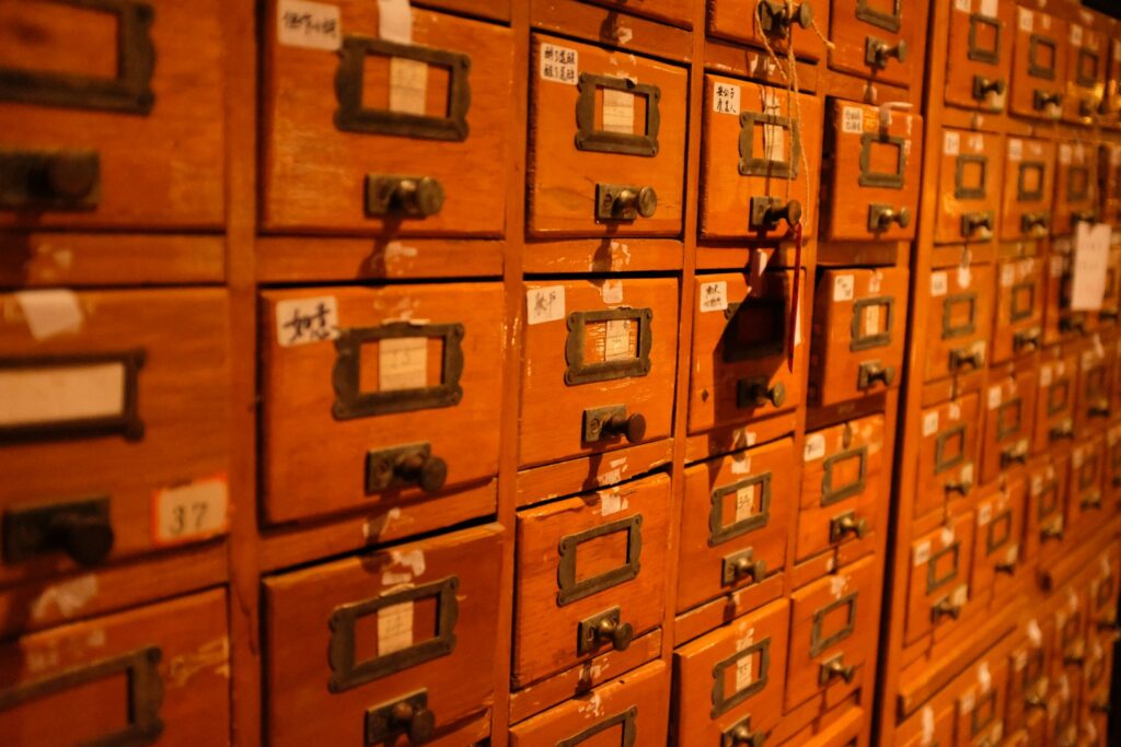 A wall of small wooden drawers with mismatched handwritten and numbered labels