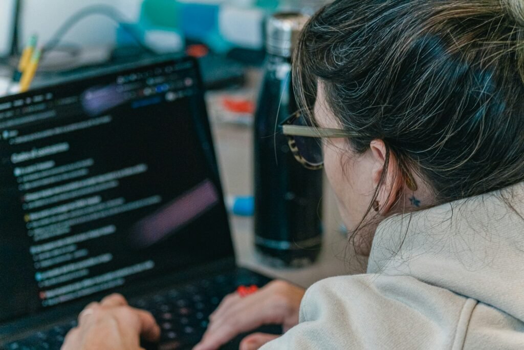 A developer in glasses working on code on a laptop at a busy desk